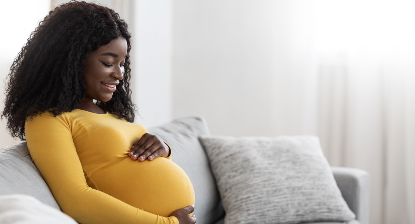 pregnant woman sitting on couch holding belly