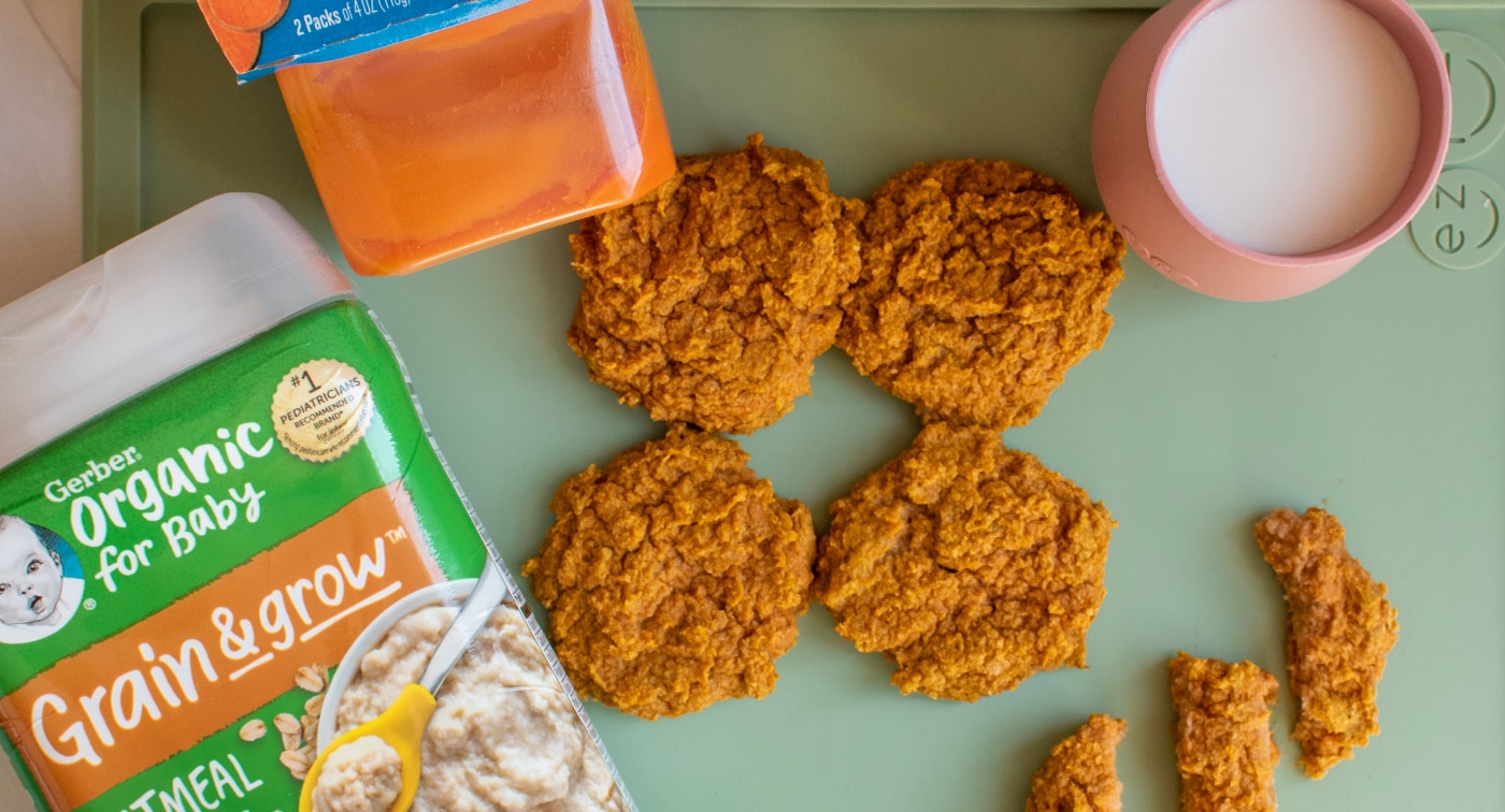 Batch of baked baby food cookies made from Gerber sweet potato puree and Gerber oatmeal banana cereal. Cookies are circular and oblong shapes arranged on a plate with a glass of milk.