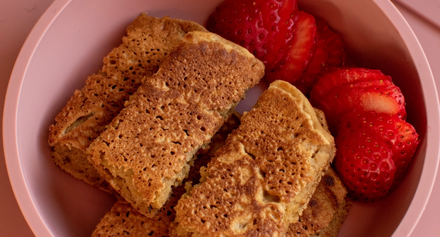 Butternut squash pancakes cut in half in a bowl with sliced strawberries.