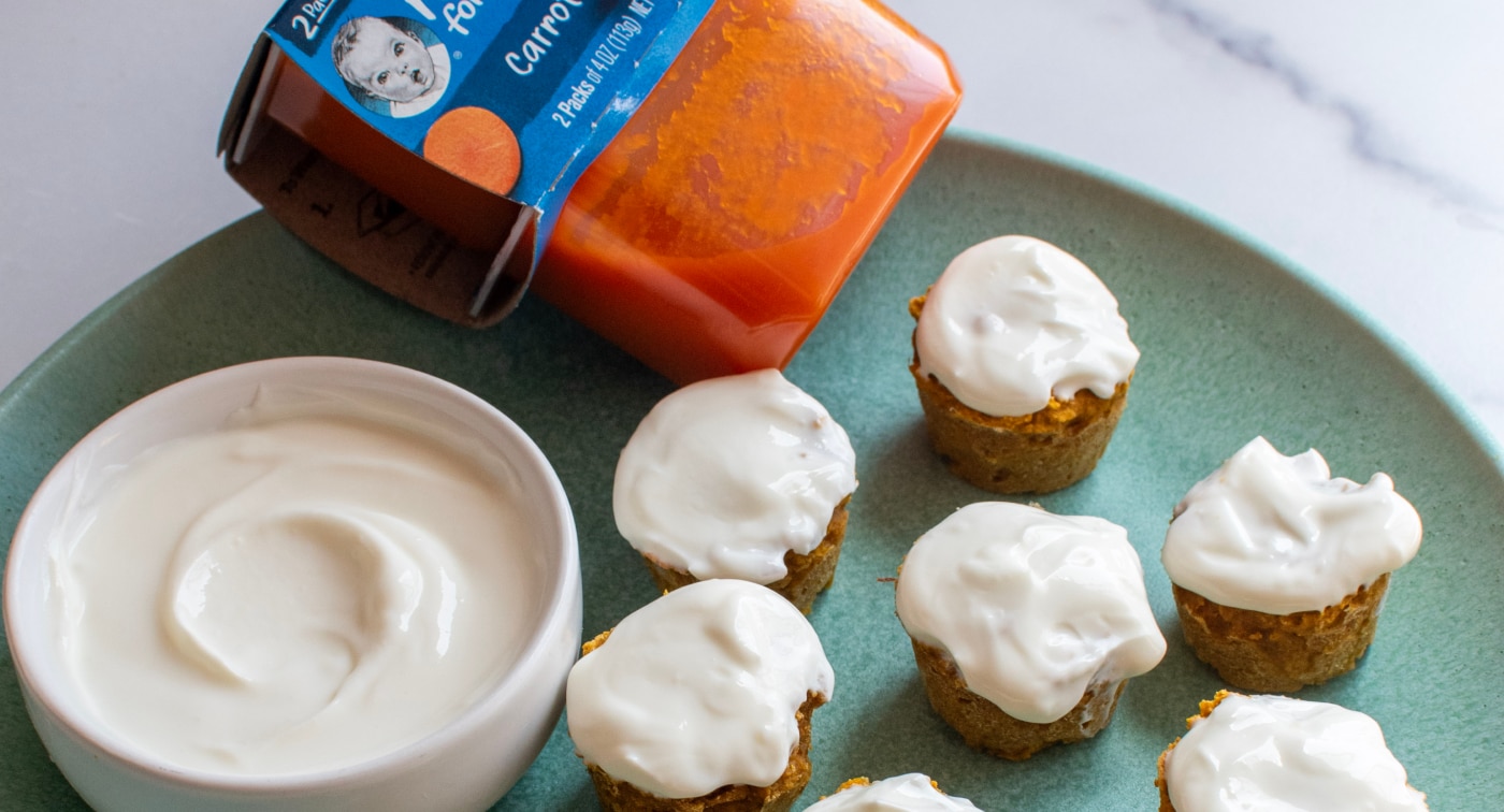 Mini carrot cake muffins made with Gerber carrot puree, topped with frosting arranged on a plate with a small bowl of frosting.