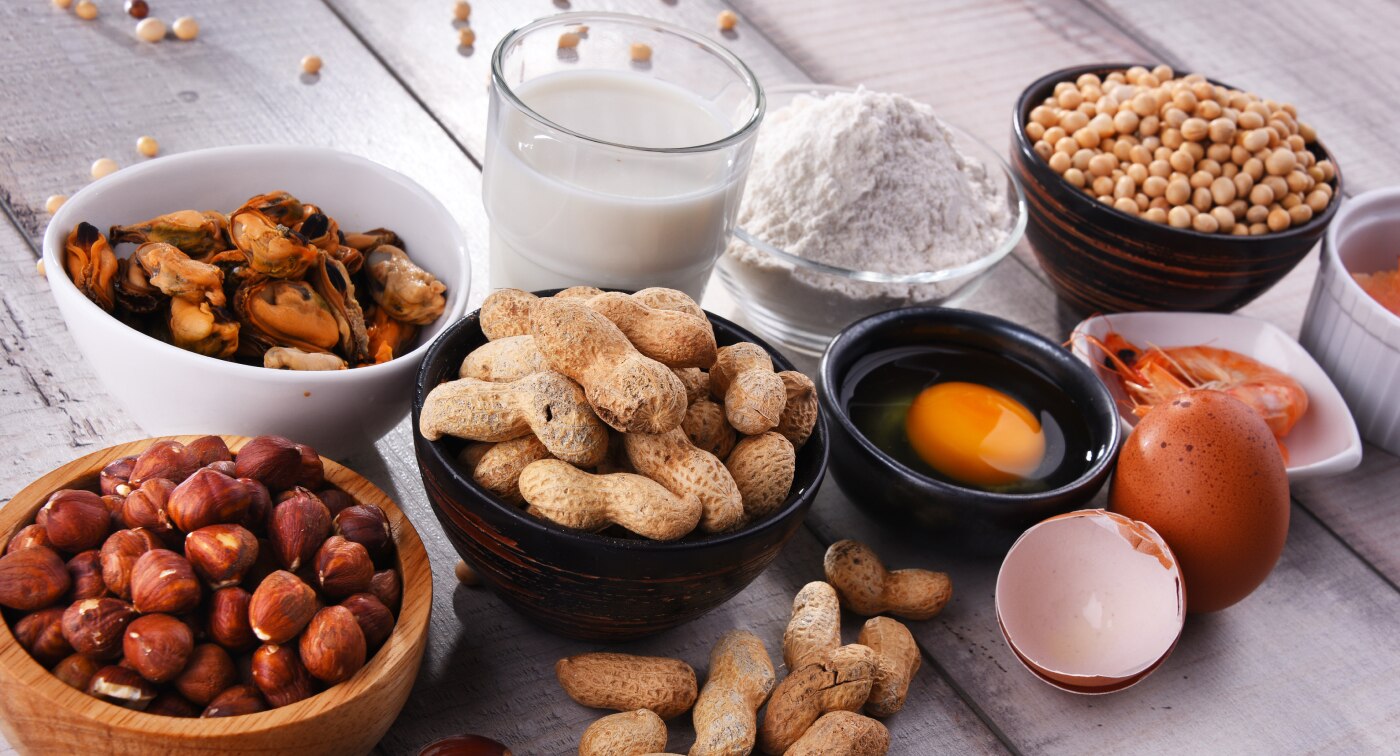 Small bowls of foods known to cause allergies including peanuts, eggs, milk, flour, and shellfish.