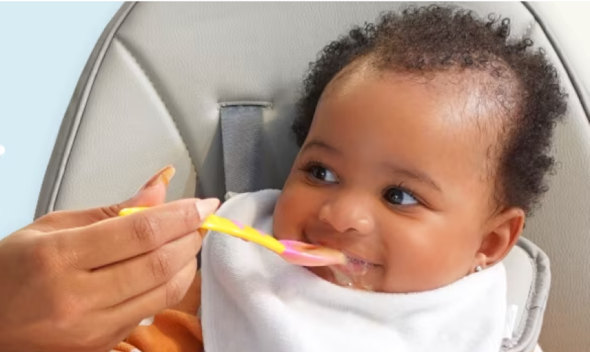 Baby sitting in high chair being spood fed baby food